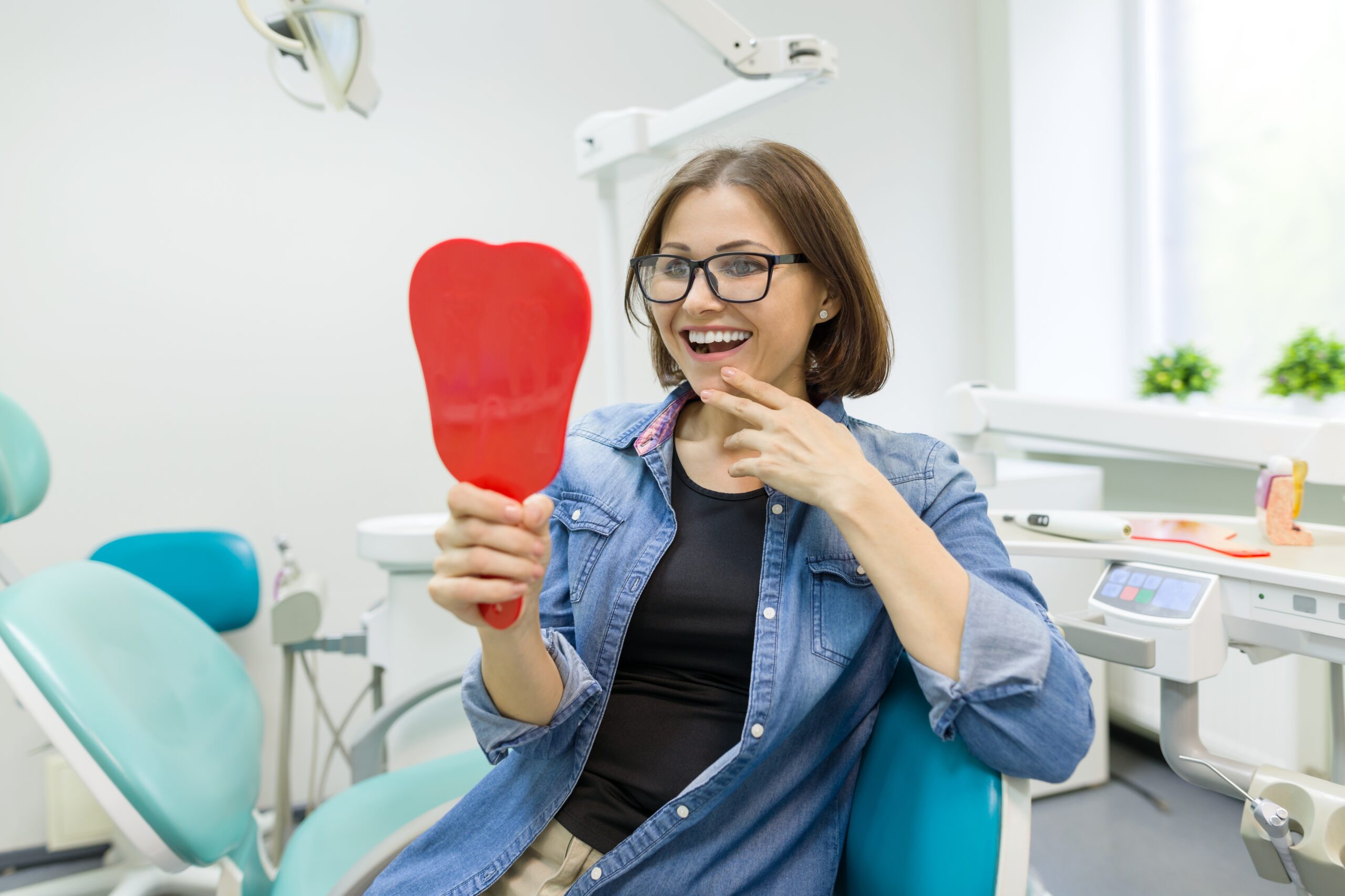 Patient smiling while looking in mirror after full-mouth reconstruction at dental office
